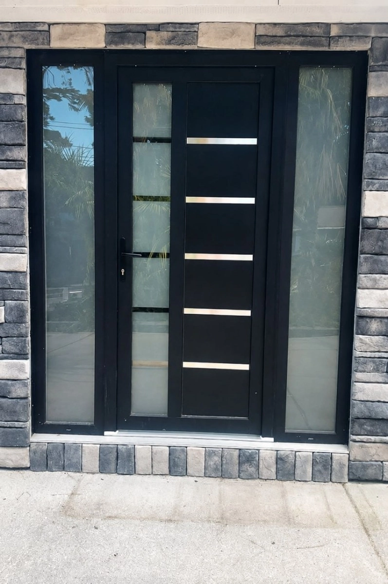 Modern matte black uPVC front door with frosted glass sidelights and a vertical glass panel, set in a grey stacked-stone exterior wall | United Porte